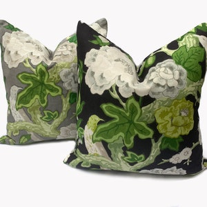 May include: Two decorative throw pillows with a floral pattern. One pillow has a black background with green and white flowers and leaves. The other pillow has a gray background with green and white flowers and leaves.