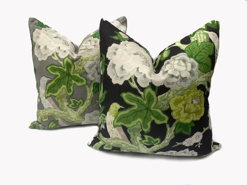 May include: Two decorative throw pillows with a floral pattern. One pillow has a black background with green and white flowers and leaves. The other pillow has a gray background with green and white flowers and leaves.