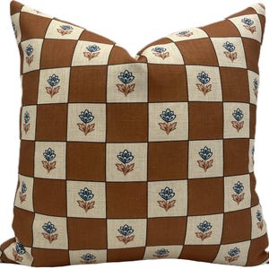 May include: Square cushion with a brown and cream chequered pattern. Each square features a blue floral design with peach accents. The cushion has a soft appearance, suitable for home decor. The dimensions are in centimetres.
