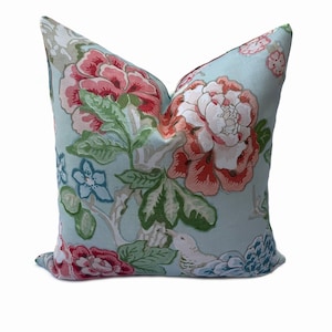 May include: A light blue pillow with a floral pattern featuring pink, red, and white flowers, green leaves, and a small bird.