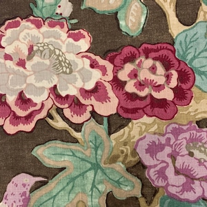 May include: A brown fabric with a floral pattern. The flowers are pink, white, and purple. The leaves are green. The fabric has a vintage look.