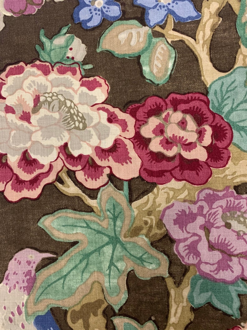 May include: A brown fabric with a floral pattern. The flowers are pink, white, and purple. The leaves are green. The fabric has a vintage look.