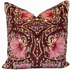 Könnte beinhalten: Ein quadratisches Kissen mit einem floralen Muster. Das Kissen hat einen burgunderfarbenen Hintergrund mit rosa Blüten, braunen Blättern und violetten Akzenten. Das Muster erinnert an den Jugendstil.