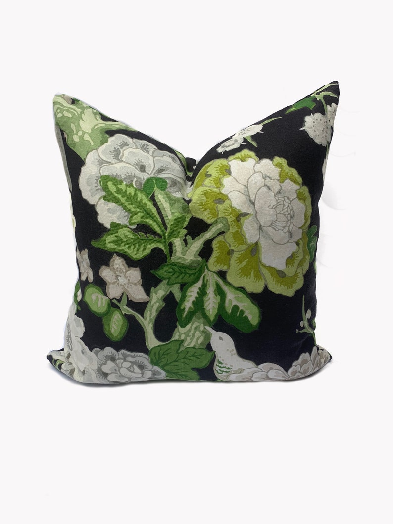 May include: Black pillow with a white and green floral pattern. The pattern features large flowers, leaves, and a small bird.