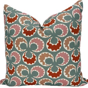 May include: Square decorative pillow with a repeating pattern of stylized, crescent-shaped designs in shades of rust, pink, tan, and white on a muted teal background. The pillow has a soft, inviting appearance, suitable for home decor.