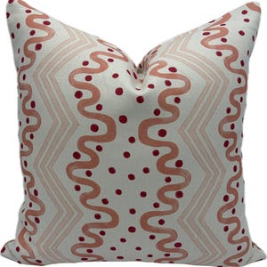 May include: Square cushion with a cream background. It features a repeating pattern of wavy lines and zigzags in a light coral colour, with small red dots scattered across. The cushion is square in shape and suitable for a sofa or bed.
