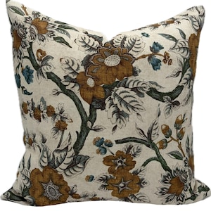 May include: Square throw pillow with a floral pattern. The pillow features a cream-colored background with a repeating design of brown and teal flowers, green stems, and leaves. The pillow has a soft, textured appearance.