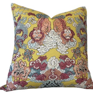 Puede incluir: Cojín decorativo amarillo con un diseño de inspiración asiática. El cojín presenta un patrón repetido de criaturas míticas, incluyendo dragones y figuras de leones, sobre un fondo de nubes y elementos florales. La paleta de colores incluye tonos de amarillo, rojo, azul y blanco.