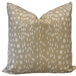 May include: A beige throw pillow with a white abstract pattern. The pillow is made of a soft, textured fabric.