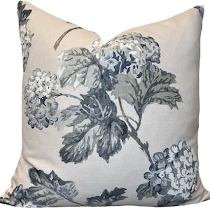 Puede incluir: Una almohada decorativa con un patrón floral que presenta hortensias azules y grises y hojas sobre un fondo beige claro.