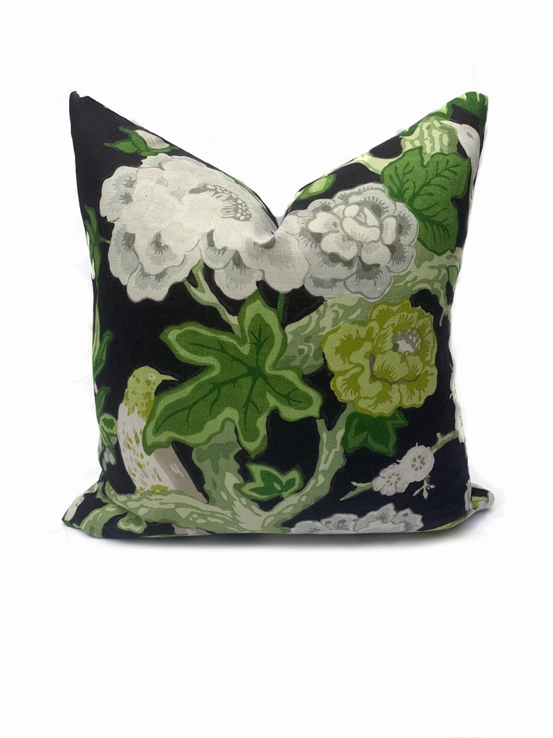May include: Black pillow with a floral pattern featuring white and green flowers, green leaves, and a white bird on a branch.