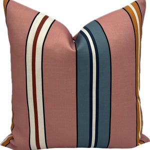 May include: A square cushion featuring a vertical striped design in shades of pink, white, navy, rust, and gold. The cushion has a textured appearance, suitable for home decor. The measurements are in centimetres.