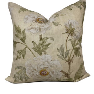 Op de afbeelding: Een beige kussen met een bloemenpatroon met witte pioenrozen en groene bladeren.