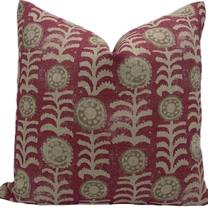 May include: A decorative throw pillow with a repeating floral pattern. The pillow features a deep red background with a beige floral design. The flowers are circular with a detailed center and are connected by a stem-like pattern.