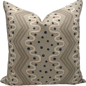 May include: Decorative square pillow with a geometric pattern. The pillow features a light beige background with a repeating design of wavy lines, zigzags, and navy blue polka dots. The pillow is a neutral color and would complement any decor.