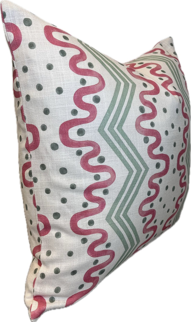 May include: A white pillow with a geometric pattern in shades of pink and green. The pattern features wavy lines, zigzags, and polka dots.