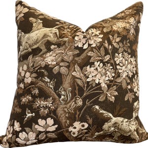 Könnte beinhalten: Ein braunes Kissen mit einem floralen und tierischen Muster. Der Druck zeigt einen Baum mit Blumen, Eichhörnchen und Hirschen. Das Kissen ist aus einem weichen, strukturierten Stoff gefertigt.