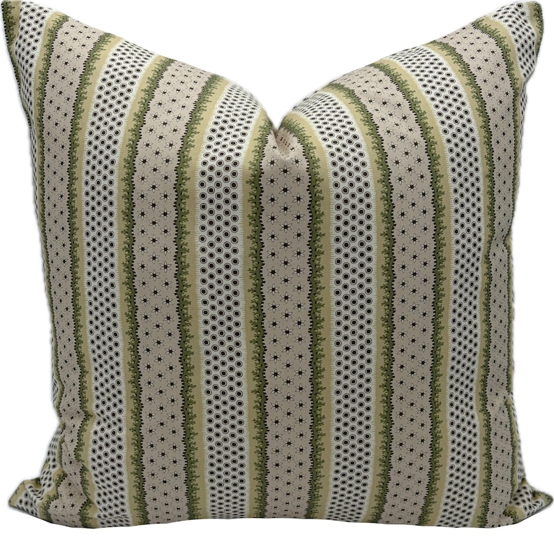 May include: A square decorative pillow with a striped pattern. The design features vertical stripes in beige, olive green, and white. The stripes alternate between dotted and floral patterns, creating a textured look. The pillow is made of a soft fabric.