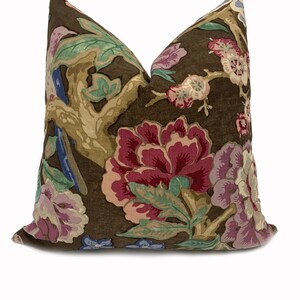 May include: A brown pillow with a floral pattern featuring pink, red, green, and blue flowers. The pillow has a brown background and a subtle linen texture.