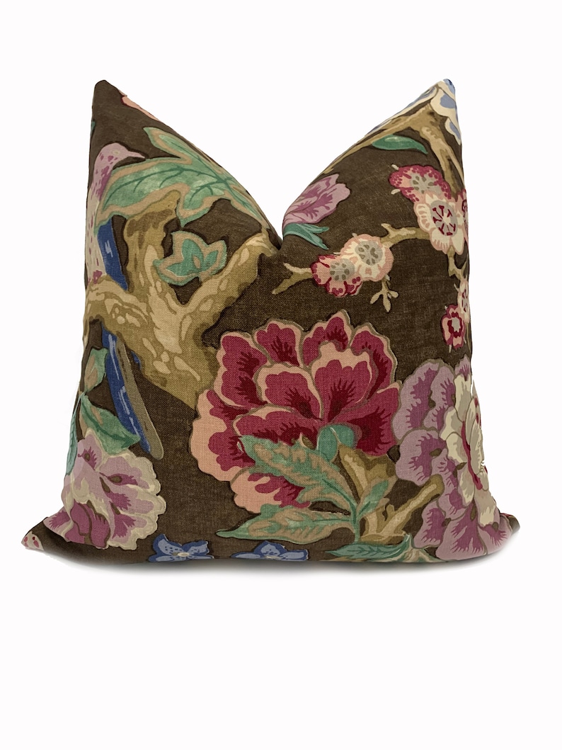 May include: A brown pillow with a floral pattern featuring pink, red, green, and blue flowers. The pillow has a brown background and a subtle linen texture.
