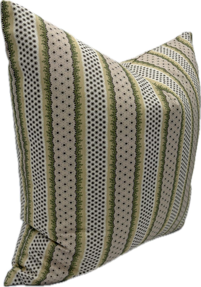 May include: A decorative pillow with a beige background and vertical stripes. The stripes alternate between patterns of small black circles, green floral designs, and tiny star-shaped flowers. The pillow is a square shape.