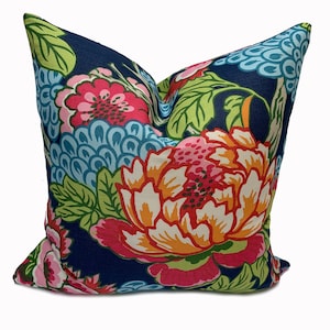 Op de afbeelding: Een donkerblauw kussen met een bloemenpatroon met grote roze, oranje en witte bloemen met groene bladeren op een donkerblauwe achtergrond.