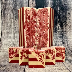 May include: Artisan soap bars with a red and white design. The larger bars have a vertical striped pattern, while the smaller bars have a diagonal pattern. The soap has a swirled, marbled appearance.