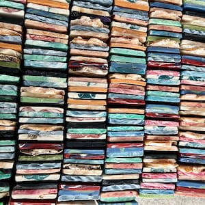 Op de afbeelding: Een close-up van een verzameling kleurrijke, rechthoekige zeepblokken. De blokken zijn in rijen gestapeld en tonen een verscheidenheid aan kleuren, waaronder groen, blauw, oranje en roze. De zeepblokken lijken handgemaakt.