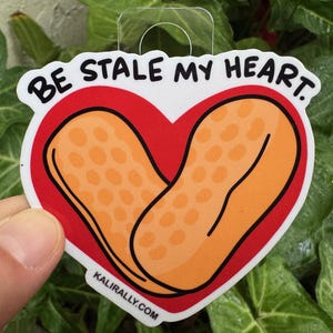 May include: A white sticker with a red heart shape containing two peanut-shaped objects. The text "BE STALE MY HEART." is above the heart. The text "KALIRALLY.COM" is below the heart.