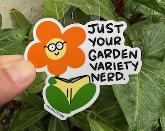 May include: A sticker featuring a cartoon flower wearing glasses and reading a book. The text "Just your garden variety nerd." is written on the sticker.