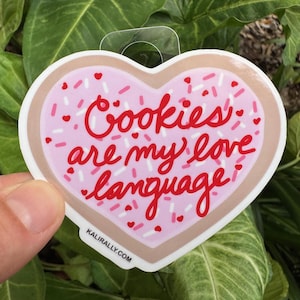 May include: Pink heart-shaped cookie sticker with white and pink sprinkles. The sticker says "Cookies are my love language".