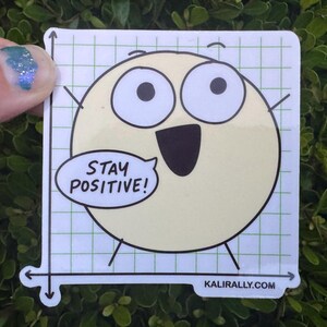 May include: A square sticker featuring a pale yellow circle character with large eyes and a wide mouth. The character is set against a green grid background with black axes. A speech bubble contains the text STAY POSITIVE! and the URL KALIRALLY.COM.