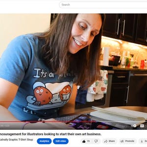 K&ouml;nnte beinhalten: Eine Frau tr&auml;gt ein blaues T-Shirt mit dem Text "It's a potato" und einer Comic-Kartoffelgrafik. Sie sitzt an einem Tisch und arbeitet an einem Laptop. Sie schaut auf den Bildschirm und l&auml;chelt.