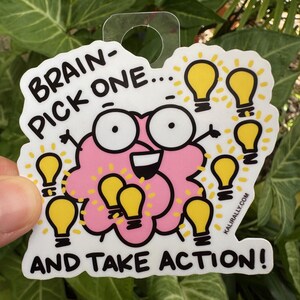 May include: A white sticker with a pink brain cartoon character with the text "Brain-Pick One... And Take Action!" and a website address "kaijirally.com". The brain has big eyes and a smile. There are light bulbs around the brain.