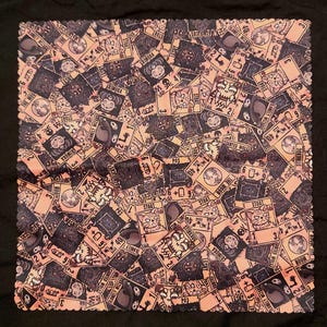 May include: A square, peach-colored cloth with a repeating pattern of illustrated playing cards. The cards feature various creatures, numbers, and text, including "STOAT", "THE MOON", and "LONELY WIZARD". The cloth is set against a black background.