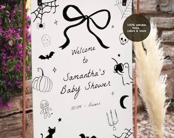 May include: A white sign with black Halloween-themed illustrations and text, including a bow, spiderwebs, and a pumpkin. The sign reads "Welcome to Samantha's Baby Shower" with the date and location. The sign is held by a copper-colored metal frame.