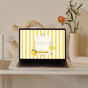 May include: A laptop displaying a webpage with yellow and white stripes, a lemon illustration, and the text "RSVP". The laptop is on a white surface, with a vase of flowers and abstract sculptures in the background.