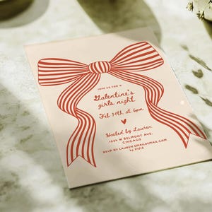 Op de afbeelding: Een Valentijnsdag uitnodiging met een groot rood strik ontwerp. De uitnodiging luidt "Galentine's girls night" en bevat de datum, tijd en locatie. Georganiseerd door Lauren.