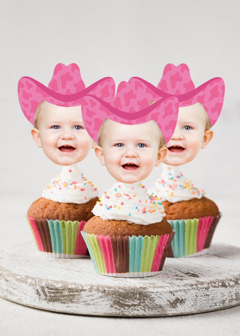 May include: Three pink and white cow print cowboy hats on top of cupcakes with white frosting and colorful sprinkles.
