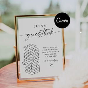 Puede incluir: Un cartel blanco con texto negro que dice "JENGA guestbook" con una ilustración en blanco y negro de una torre de Jenga. El cartel está en un marco dorado y está sentado sobre una superficie de madera. El texto debajo de la ilustración dice "PLEASE HELP US BUILD MEMORIES! SIGN A PIECE WITH WELL WISHES FOR THE NEW mr & mrs wifflang".