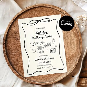 May include: A cream-colored Pilates birthday party invitation with black line art illustrations of exercise equipment and text. The invitation is on a wooden tray with a white cloth and dried flowers.