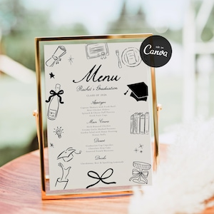 May include: A graduation menu displayed in a gold frame. The menu features black line art illustrations and text, including the name "Rachel's Graduation" and the class year "2026". The menu lists appetizers, main courses, desserts, and drinks.