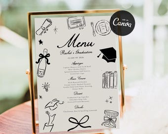 May include: A graduation menu displayed in a gold frame. The menu features black line art illustrations and text, including the name "Rachel's Graduation" and the class year "2026". The menu lists appetizers, main courses, desserts, and drinks.