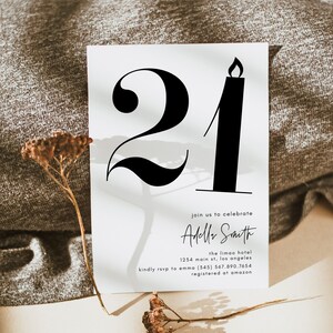 May include: A white invitation card with black text and a large black number "21" with a candle flame on top. The text reads "Join us to celebrate Adele Smith, the Limao Hotel, 1234 Main St, Los Angeles, kindly rsvp to Emma (345) 567.890.7654, registered at Amazon."