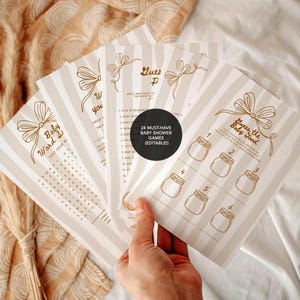 May include: A collection of baby shower games with a beige and white striped design. The games feature a word search, a guessing game, and other activities. The text is in brown. The games are held in a hand.