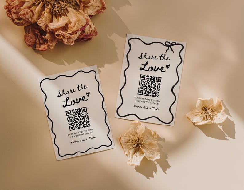 May include: Two white cards with black wavy borders and the text "Share the Love" with a QR code and the text "Scan the code to share your photos with us!" and the names "xoxo, Lia + Mike". Dried flowers are scattered around the cards.