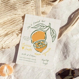 May include: A lemon-themed bridal shower invitation featuring a hand-drawn illustration of lemons and the text "She's found her main squeeze". The invitation includes the bride's name, the date and time of the shower, the location, and the registry information.