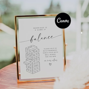Puede incluir: Un cartel blanco en un marco dorado con el texto "Marriage is a game if balance" y una ilustración en blanco y negro de un juego de Jenga. El cartel también incluye el texto "Please help us build memories! Sign a piece with well wishes for the new mr & mrs wifflang ♡".