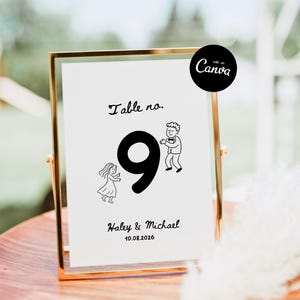 May include: A gold-framed table number sign with the number 9 in a large, bold font. The sign includes the text "Table no." and the names "Haley & Michael" with a date. The sign has a cartoon illustration of a dancing couple.