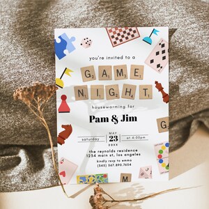 May include: A white invitation card with colorful illustrations of game pieces and a white background. The text reads "You're invited to a Game Night housewarming for Pam & Jim, Saturday, May 23, 20XX at 4:00pm, The Reynolds Residence, 1234 Main St, Los Angeles, Kindly RSVP to Emma (345) 567.890.7654".